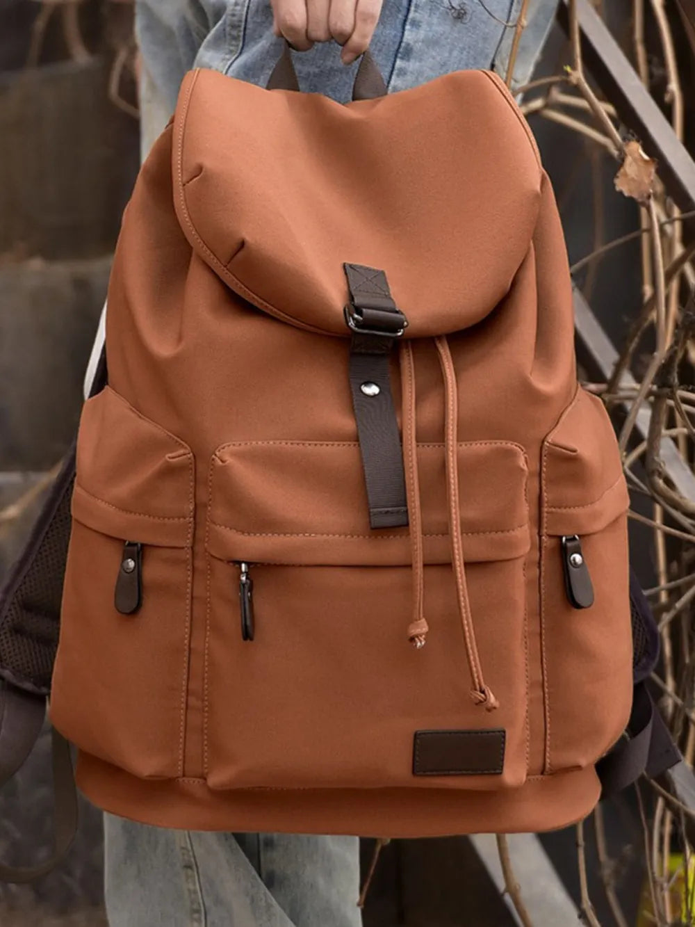 Ochre canvas backpack with flap buckle, drawstring pulls, and side zip pockets