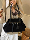 Black suede shoulder bag with buckle strap, top handles, and hanging charm tag