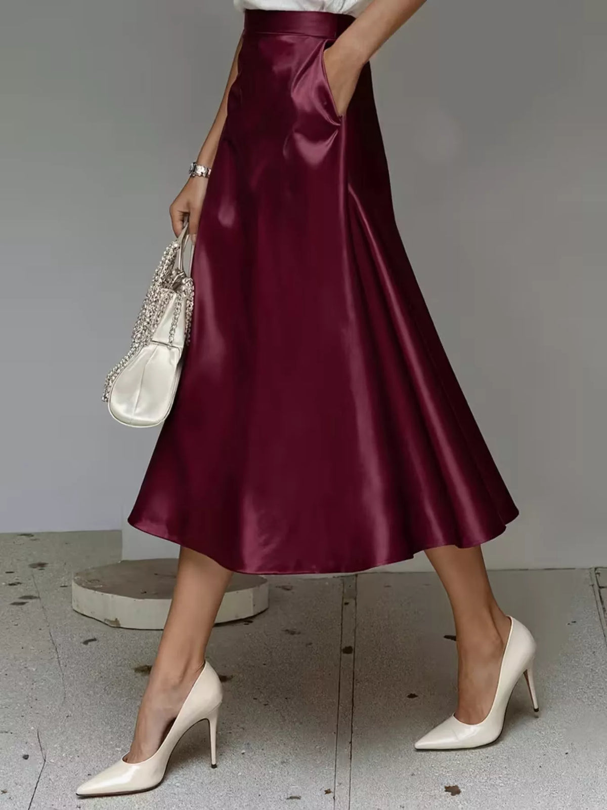 High-waist satin midi skirt in wine red, flowing flared hem and glossy fabric.