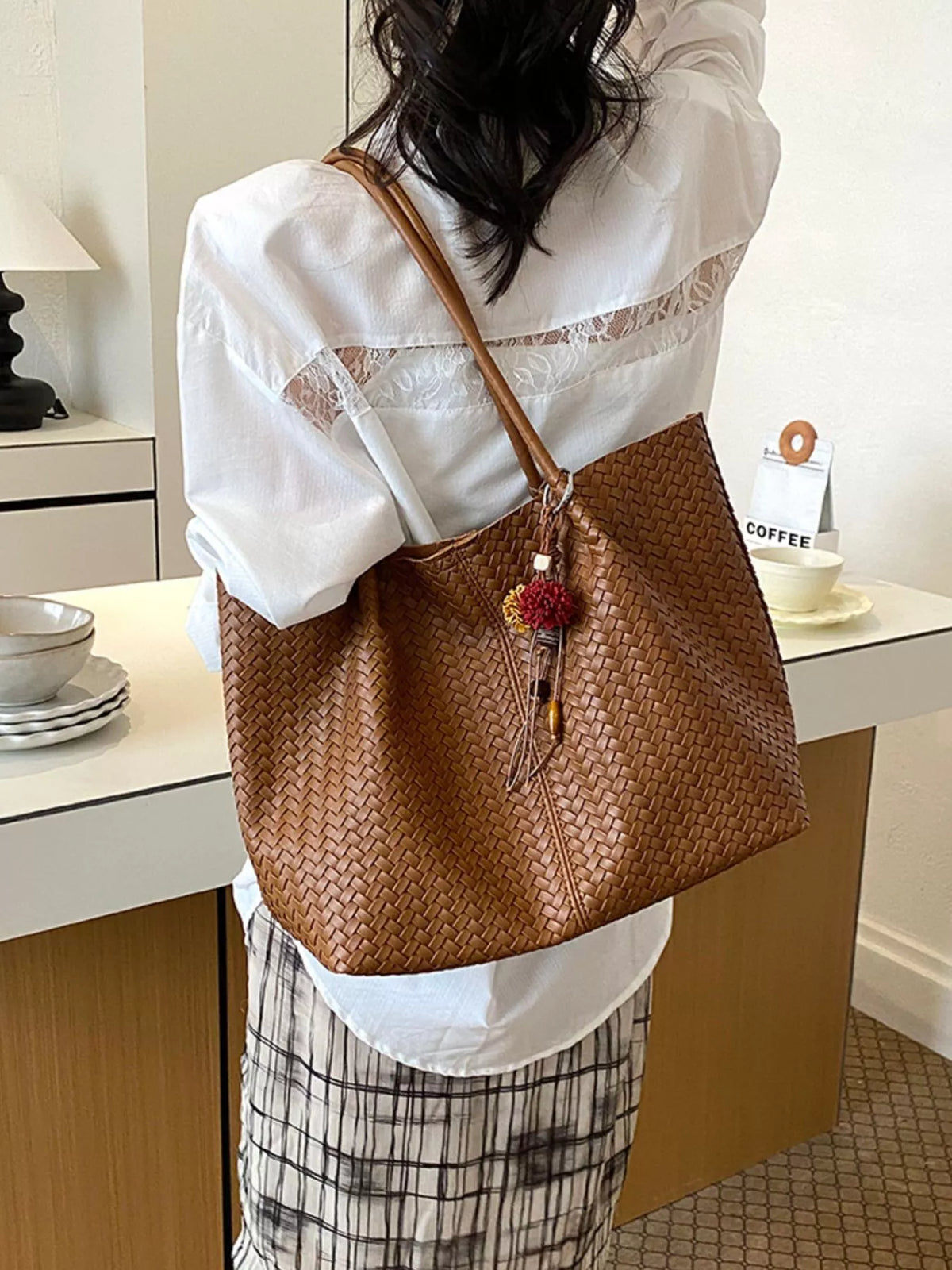 Brown woven vegan leather tote bag with long strap handles and floral tassel charm