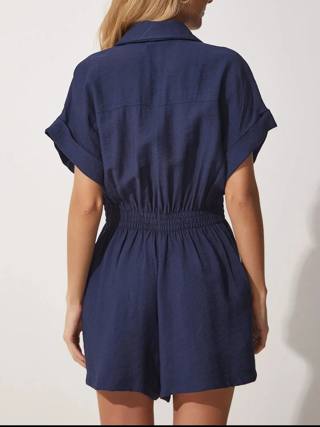 Back view of dark blue short-sleeve romper with collar and cinched elastic waist.