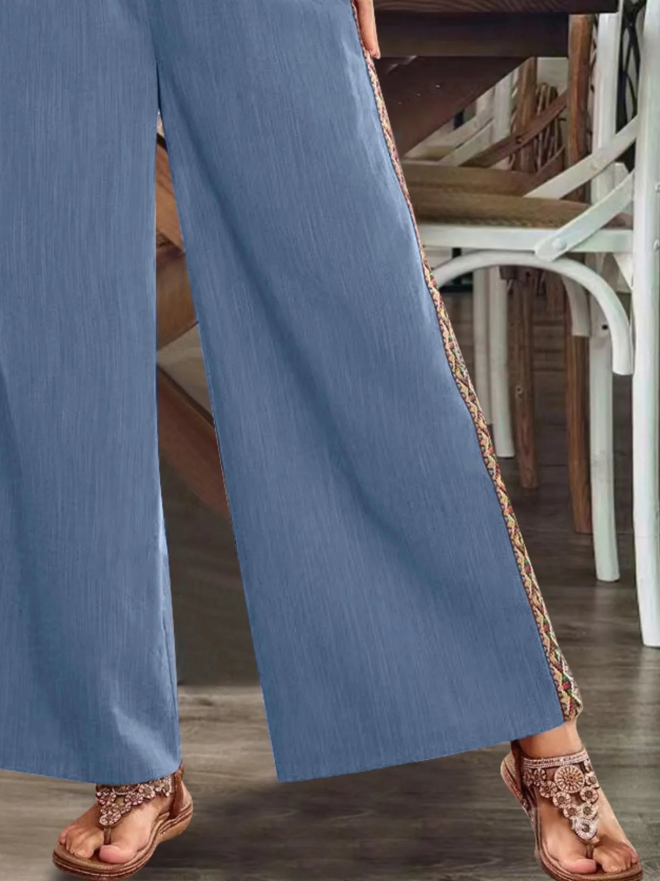 Close-up of blue wide-leg pants with embroidered side stripe and flared hem.