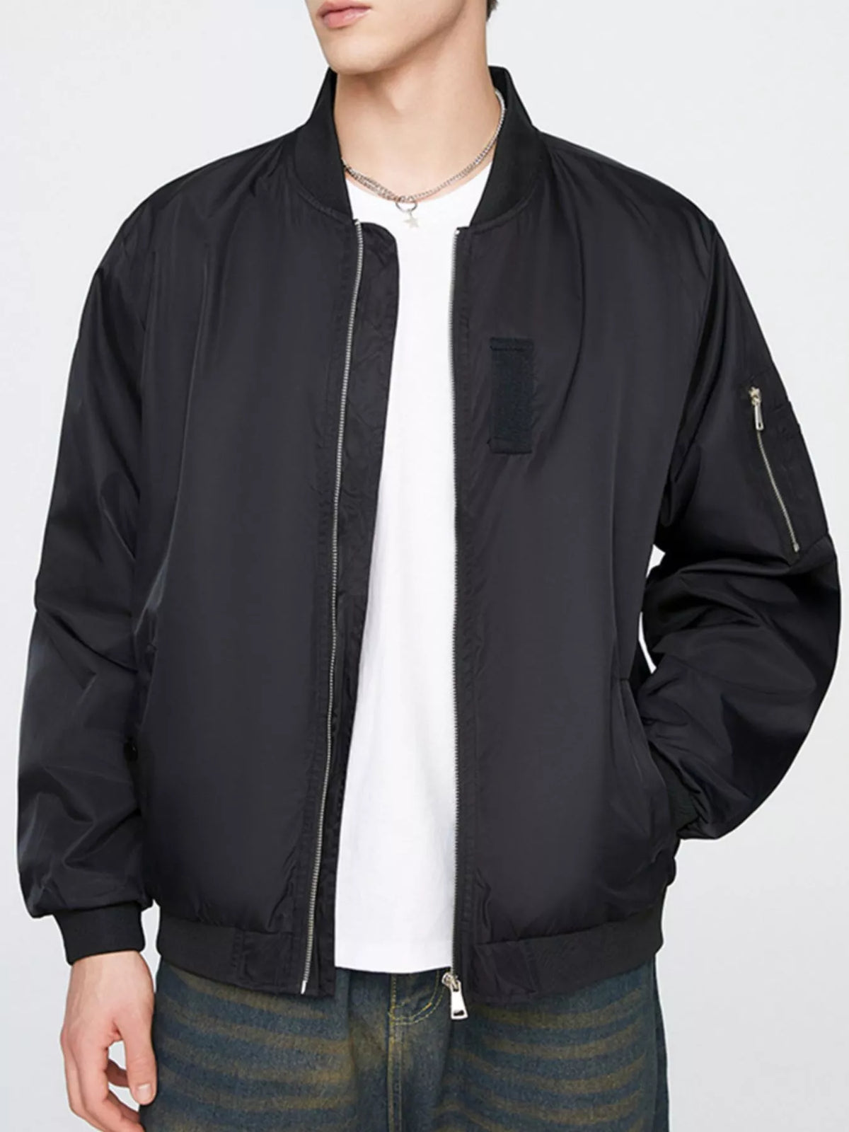Black lightweight bomber jacket with front zip, ribbed hem, and zip pocket on the sleeve
