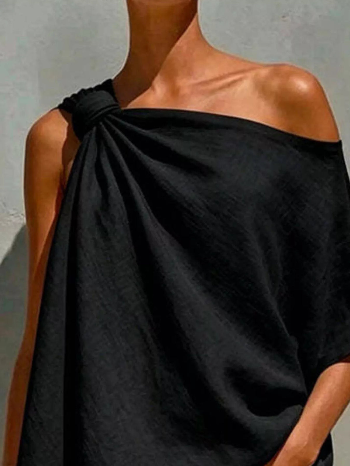 Black one-shoulder blouse close-up with knotted neckline and flowing draped fabric