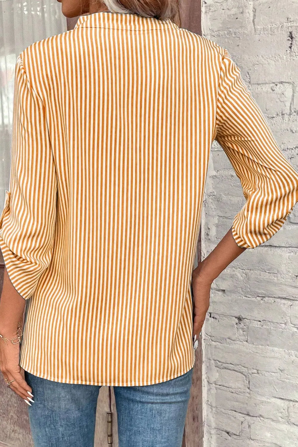 Back view of gold and white striped shirt with roll-tab sleeves and relaxed fit