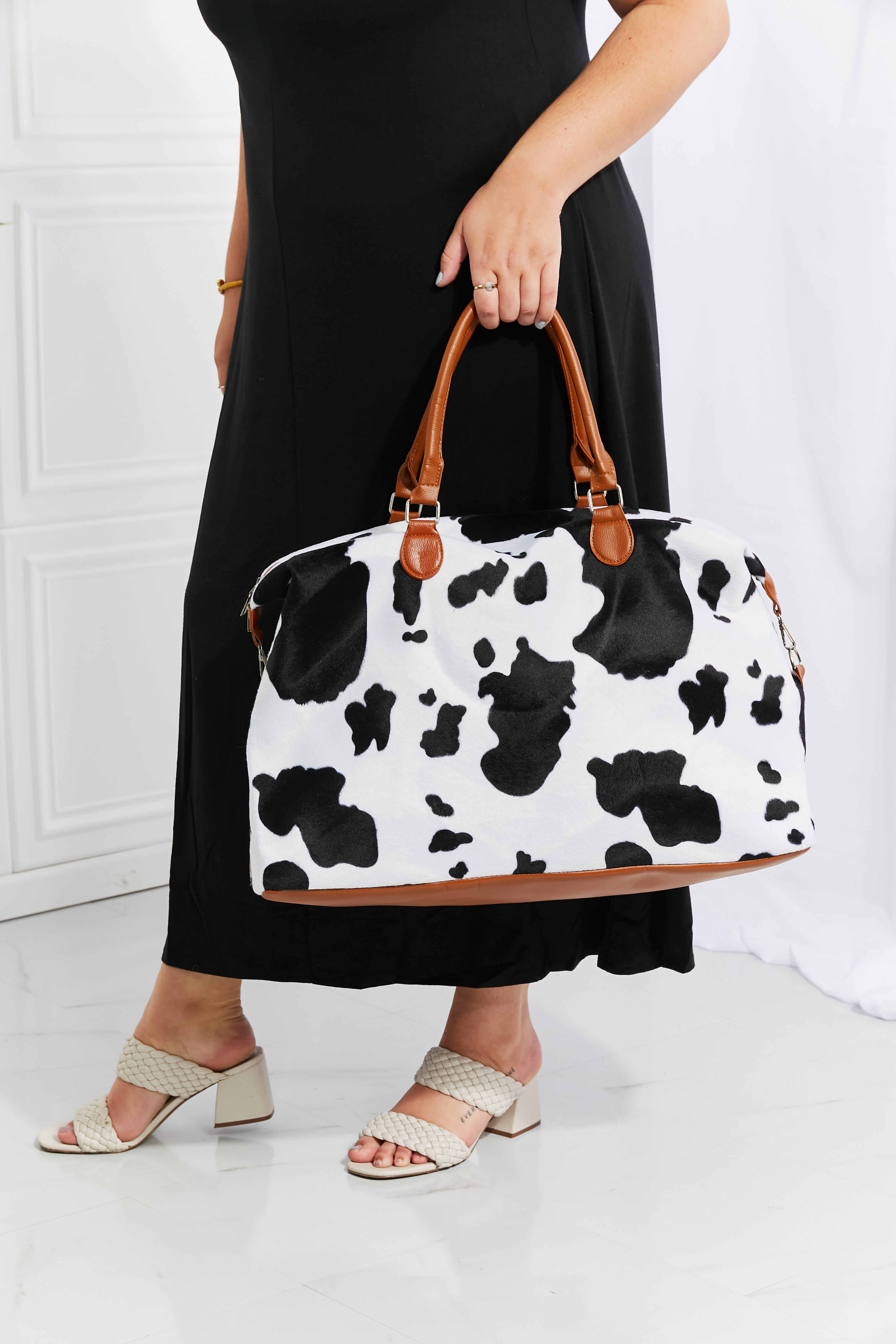 Cow print plush weekender bag with tan leather-look handles and zip top