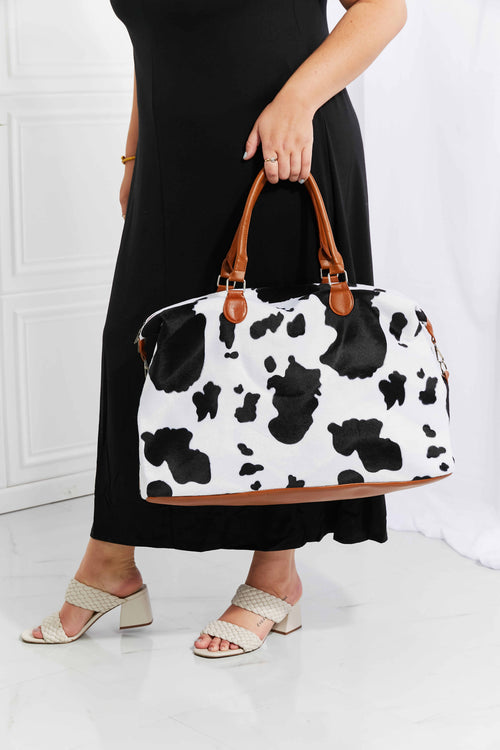 Cow print plush weekender bag with tan leather-look handles and zip top