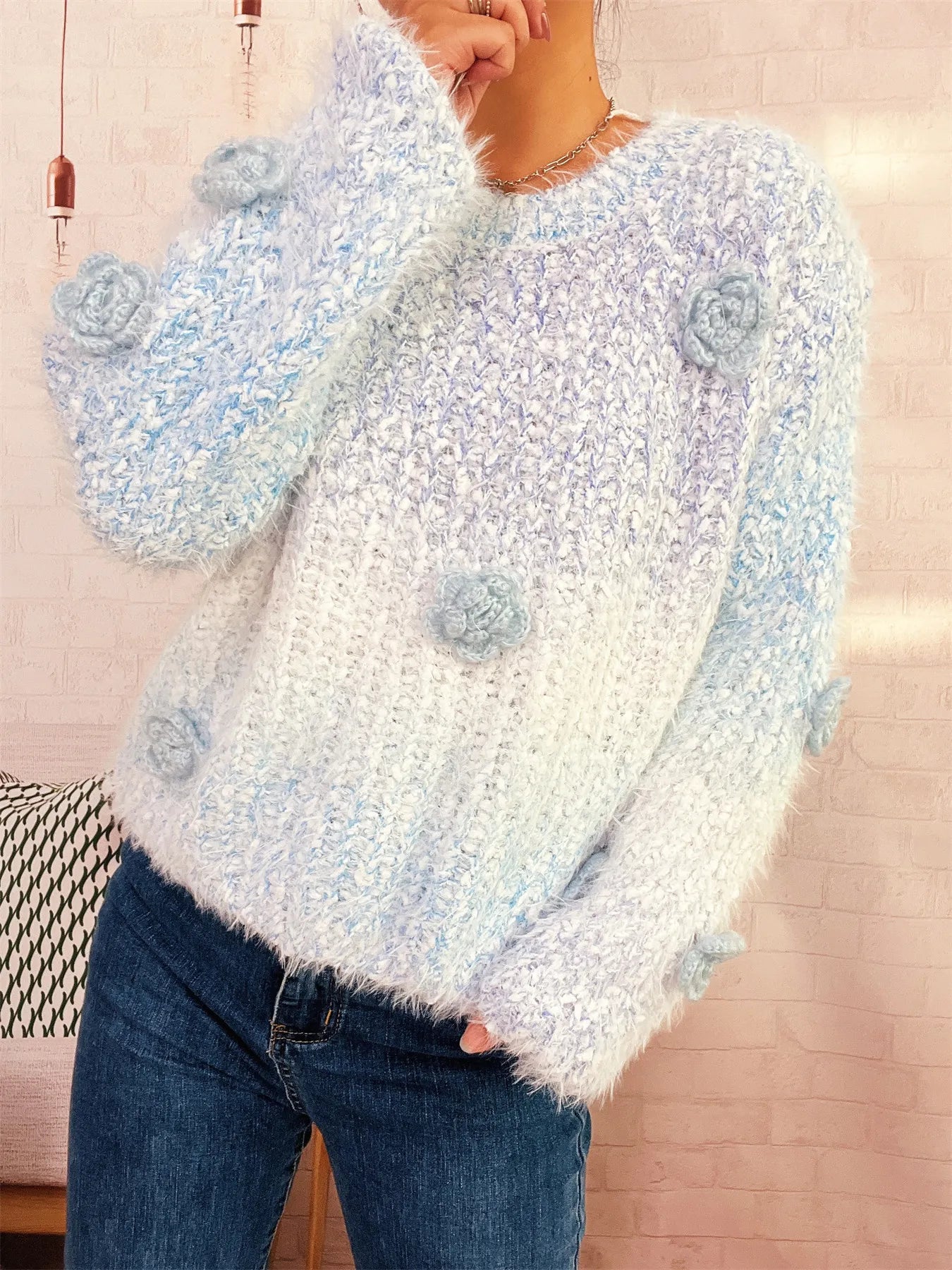 Light blue fuzzy knit sweater with round neck and flower appliques, arm raised.