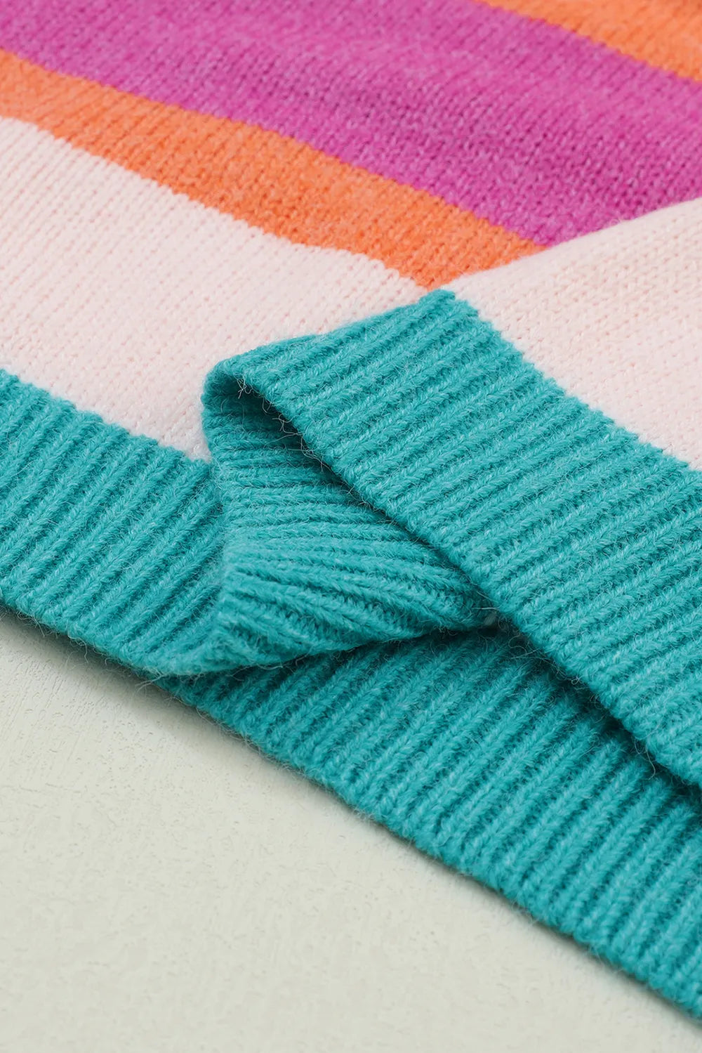 Knit cuff detail on a multicolor striped sweater with teal ribbing at the sleeve end.