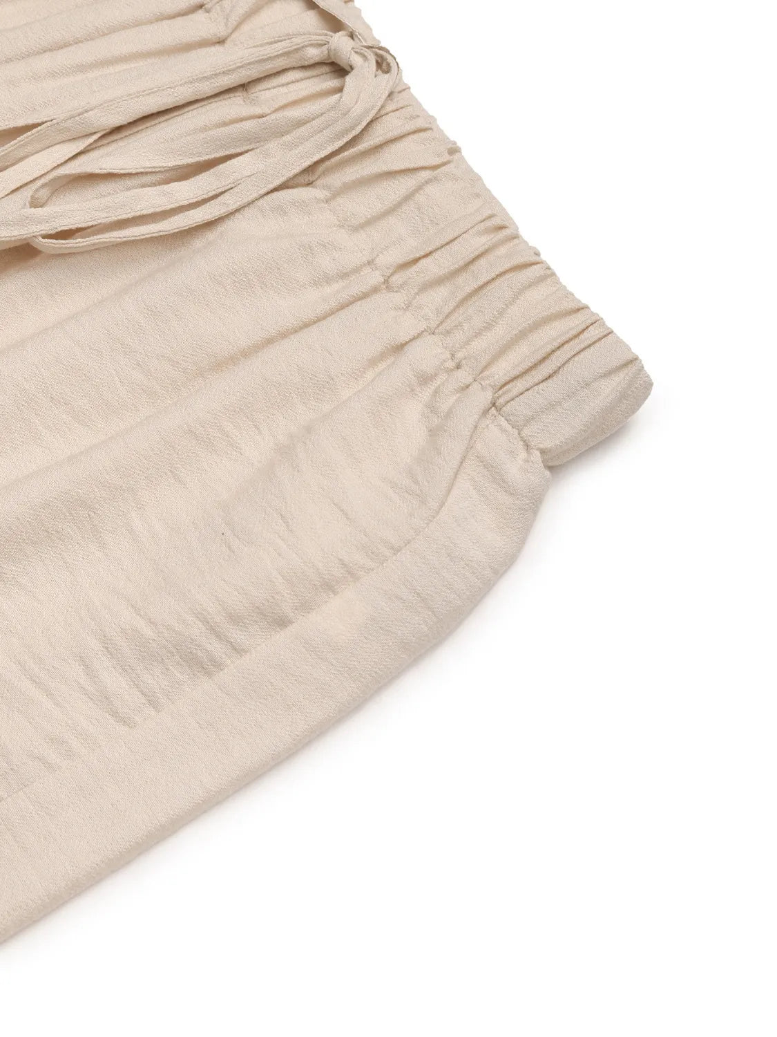Cream textured pant fabric with soft drape and lightly gathered folds near waist