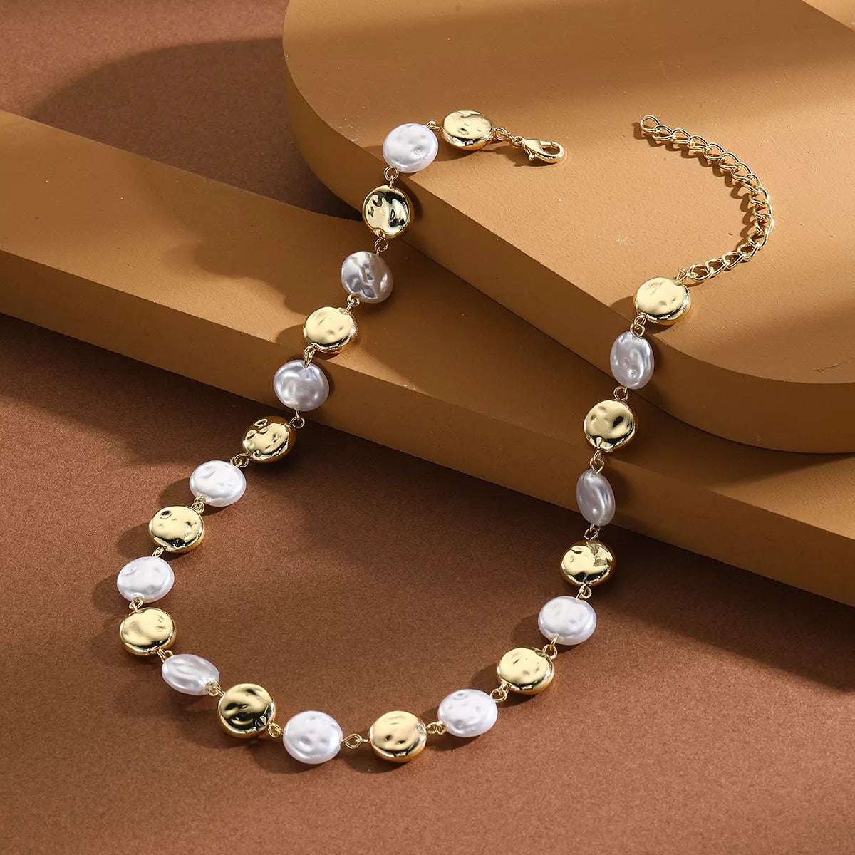 Pearl chain necklace with gold-tone coin beads and white pearl beads, side view on stand