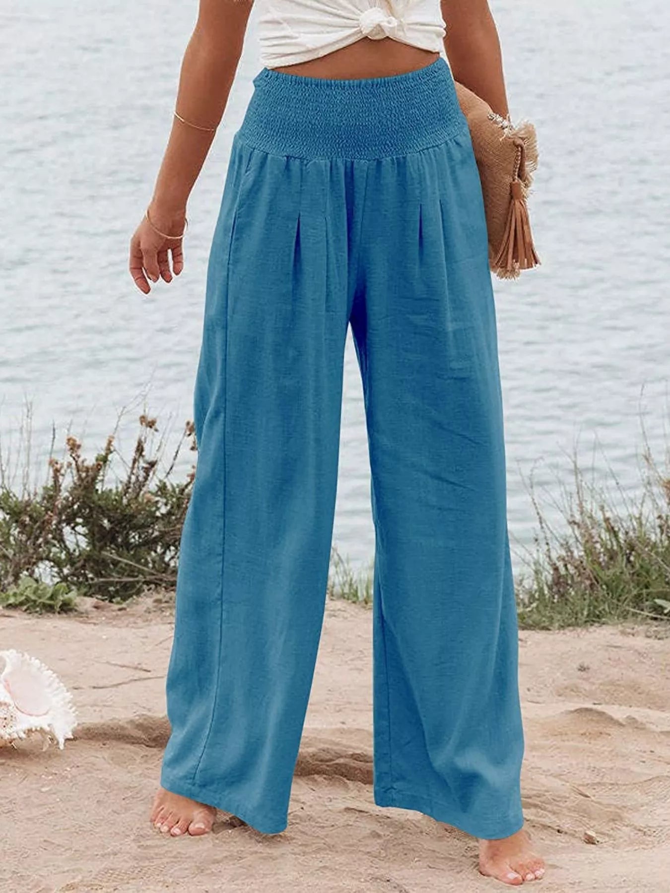 Sky blue smocked high-waist wide-leg pants with soft, loose drape.