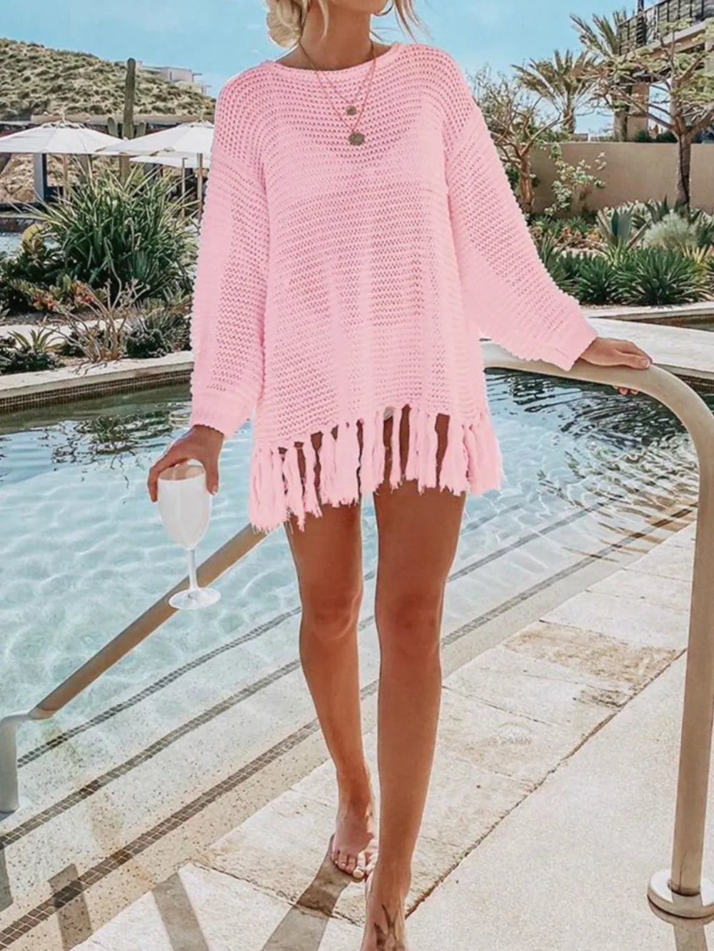 Blush pink long-sleeve openwork knit cover up with tassel fringe hem.
