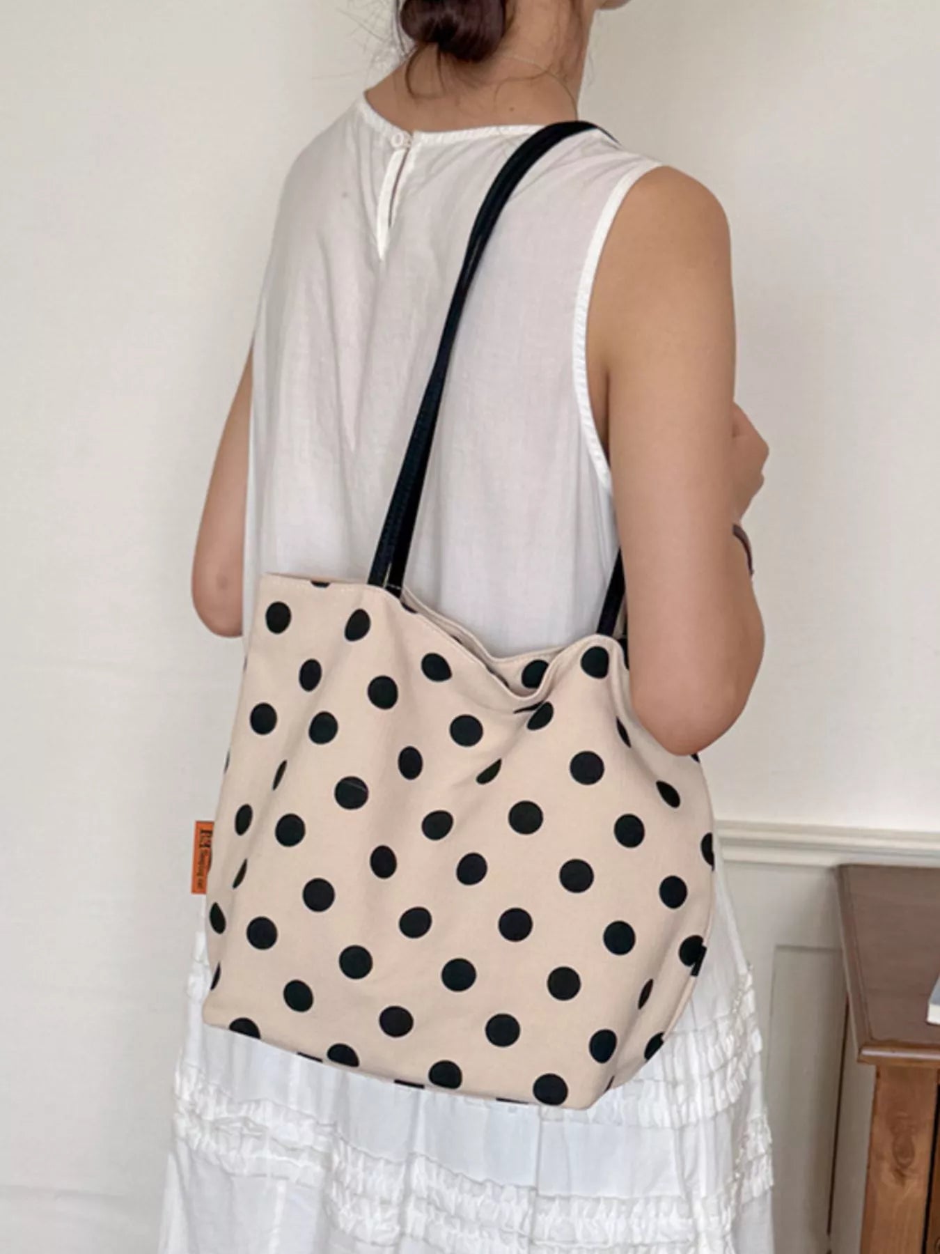 Cream polka dot shoulder bag with black dots, black strap, and rounded top silhouette