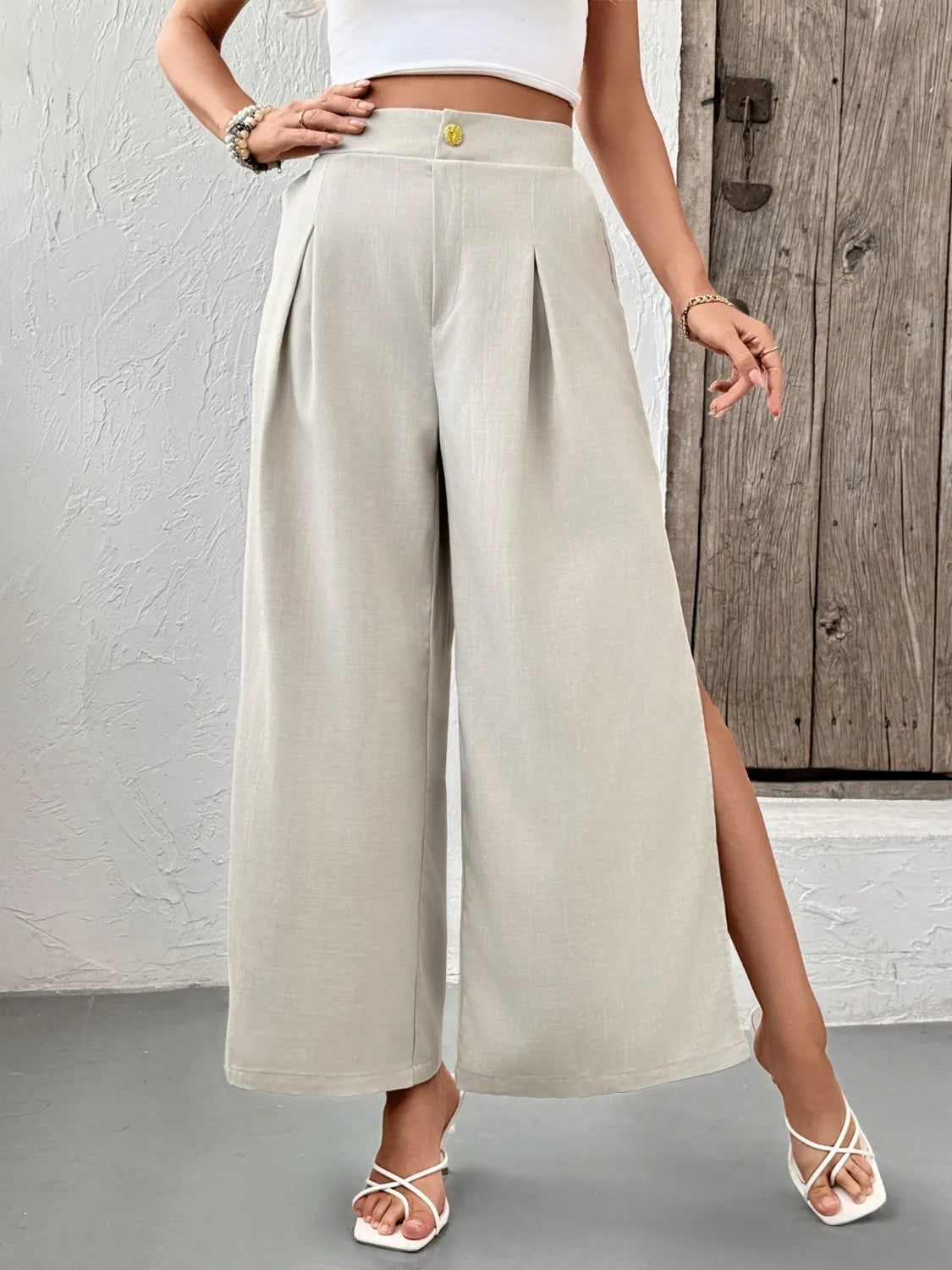 Beige wide-leg pleated pants with deep side slits and front crease pleats