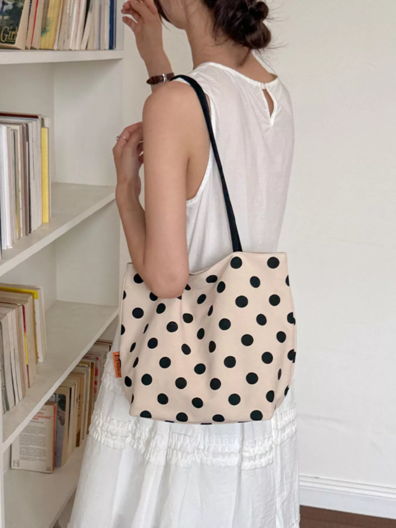 Cream polka dot tote bag with black dots and black handles, side view with pocket detail