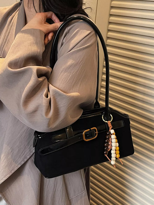 Black shoulder bag with front buckle, top handle, and hanging beaded charm
