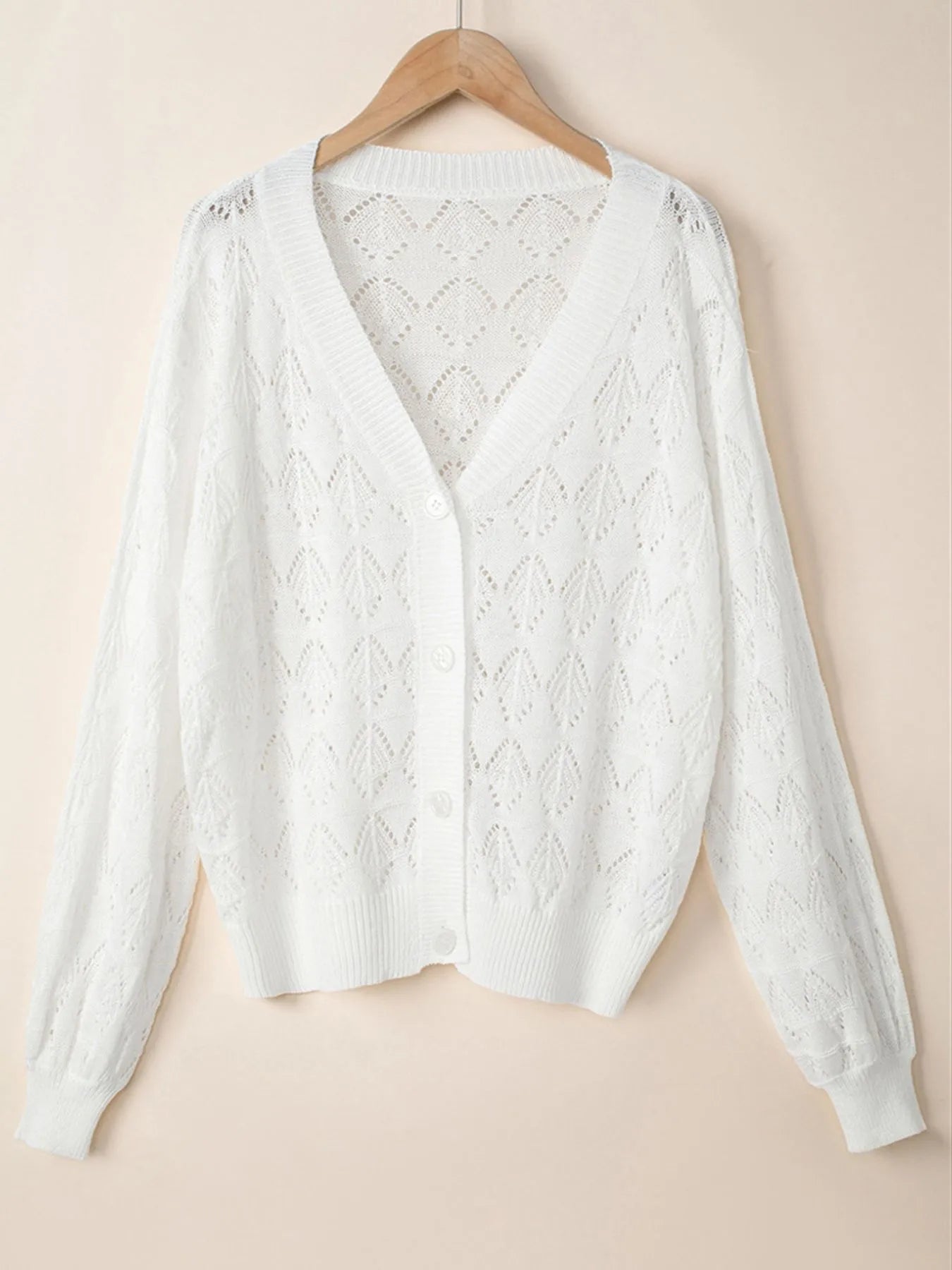 White openwork button-up cardigan with V-neck and long sleeves, hanging on hanger