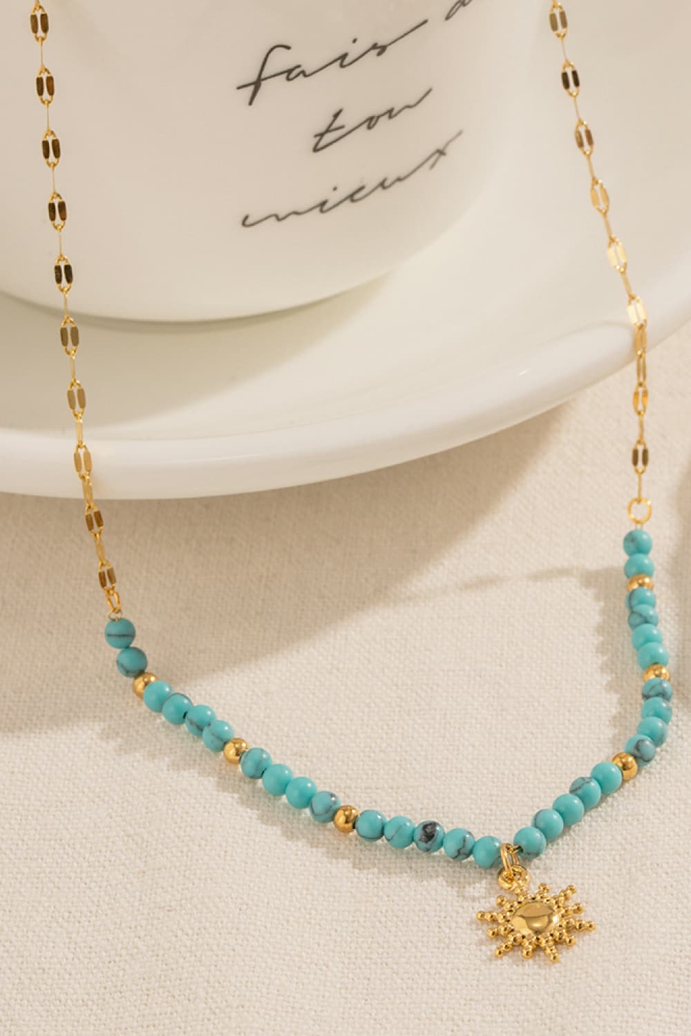 Turquoise bead and gold link pendant necklace with sun charm at the bottom