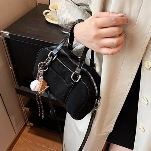 Black crossbody bag held open with silver buckles and chain charm