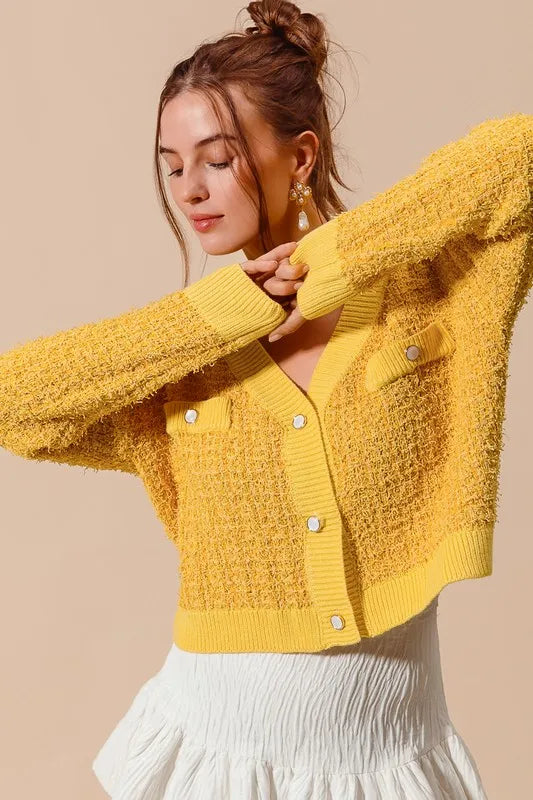 Mustard yellow knit cardigan with button front and textured cuffs, arms raised