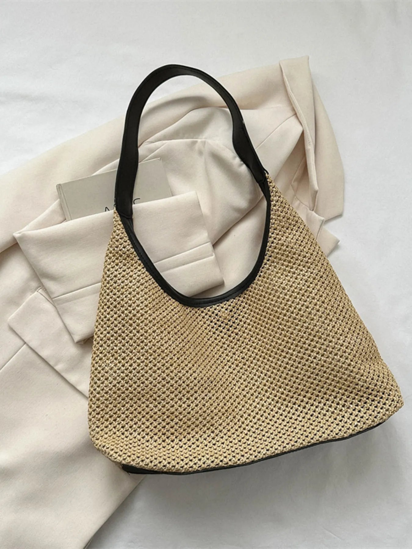 Woven straw shoulder bag in tan with black top handles, rounded open-top hobo