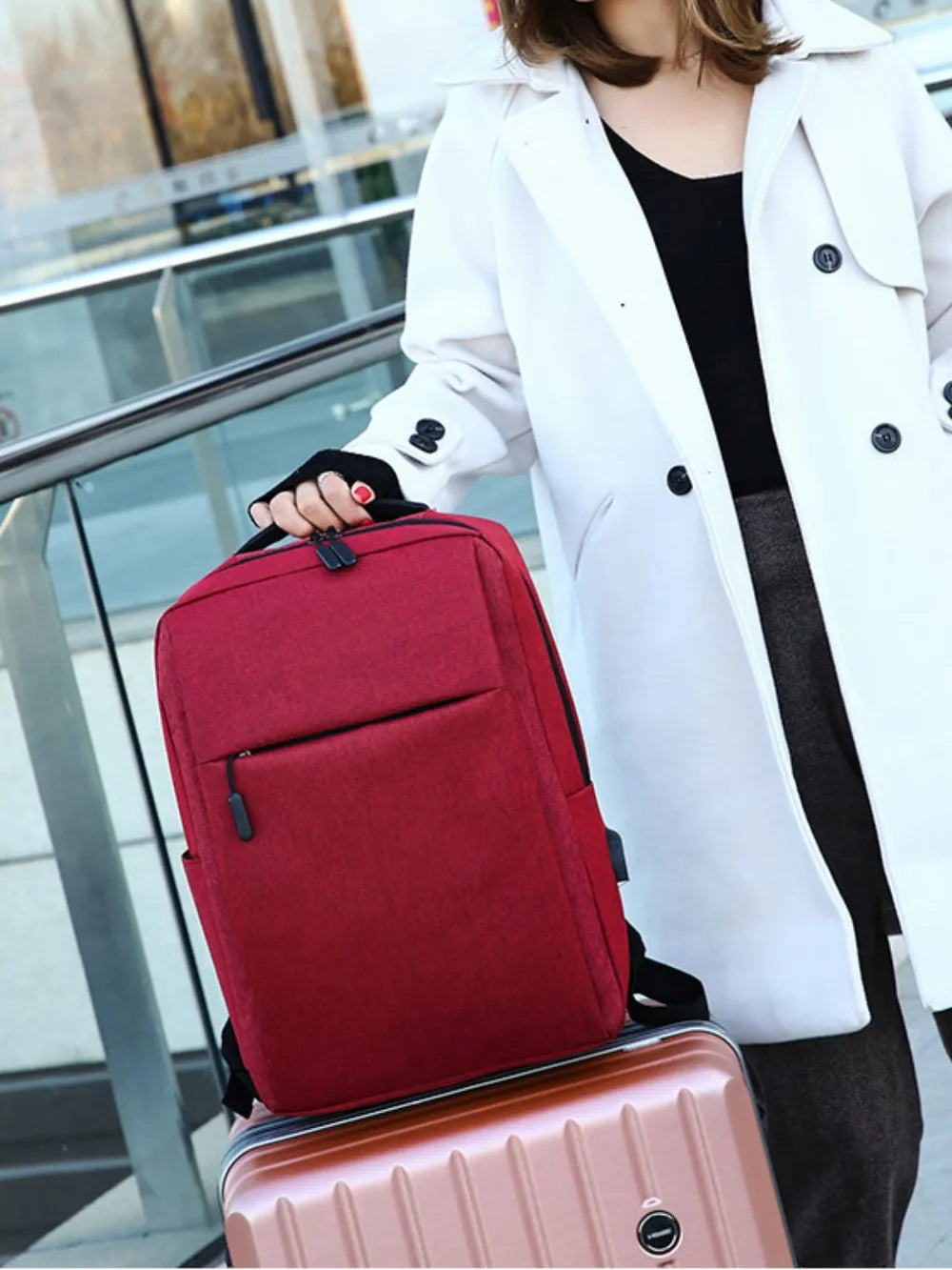 Burgundy backpack with front zip pocket and adjustable shoulder strap worn by a person.