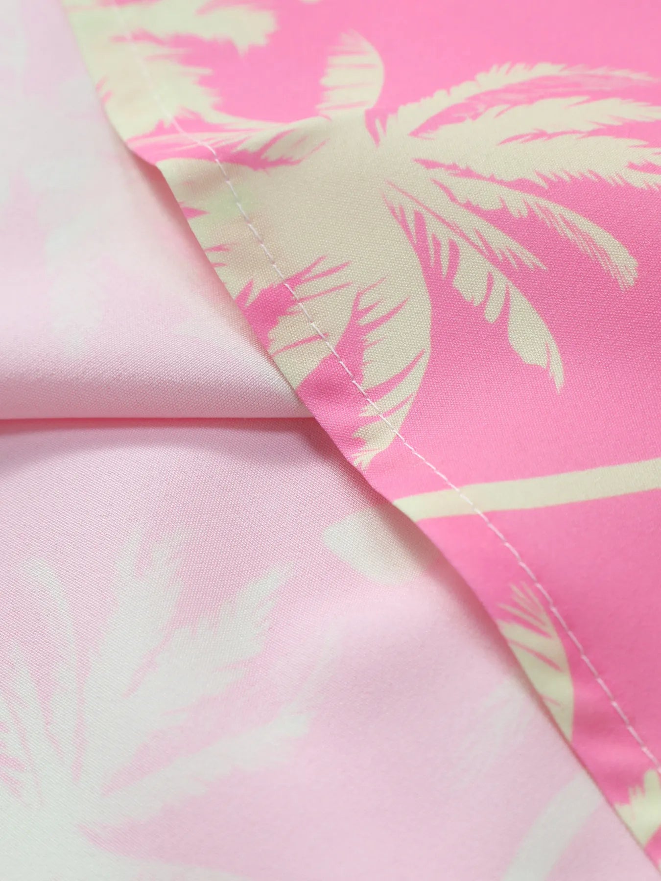 Dusty pink palm print shirt fabric close-up with stitched edge