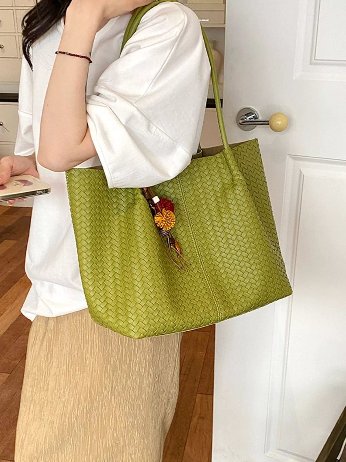 Green woven vegan leather tote bag with long handles, zipper top, and tassel charm