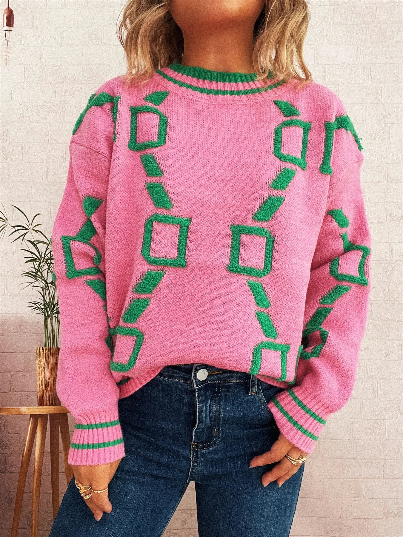 Pink long-sleeve sweater featuring green geometric squares and ribbed round neckline