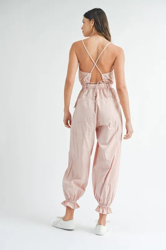 Pink backless jumpsuit with crisscross straps, waist tie belt, and gathered jogger cuffs