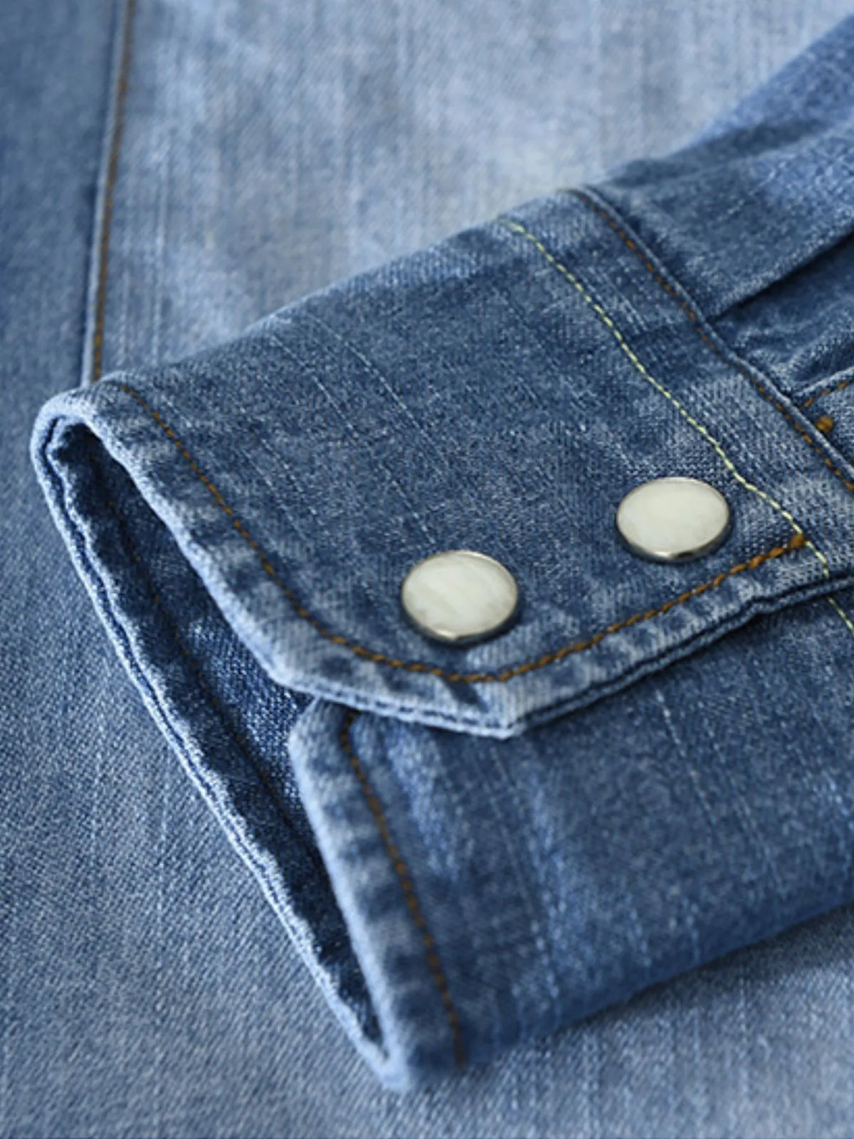 Men's denim button-up shirt cuff with two snap buttons and contrast stitch, dark blue