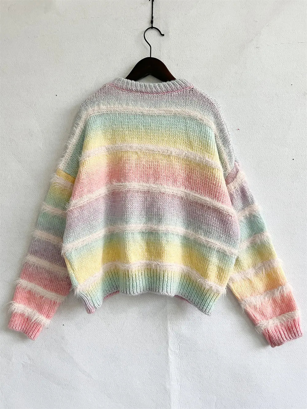 Striped round-neck long-sleeve sweater on a hanger, soft pastel rainbow horizontal stripes