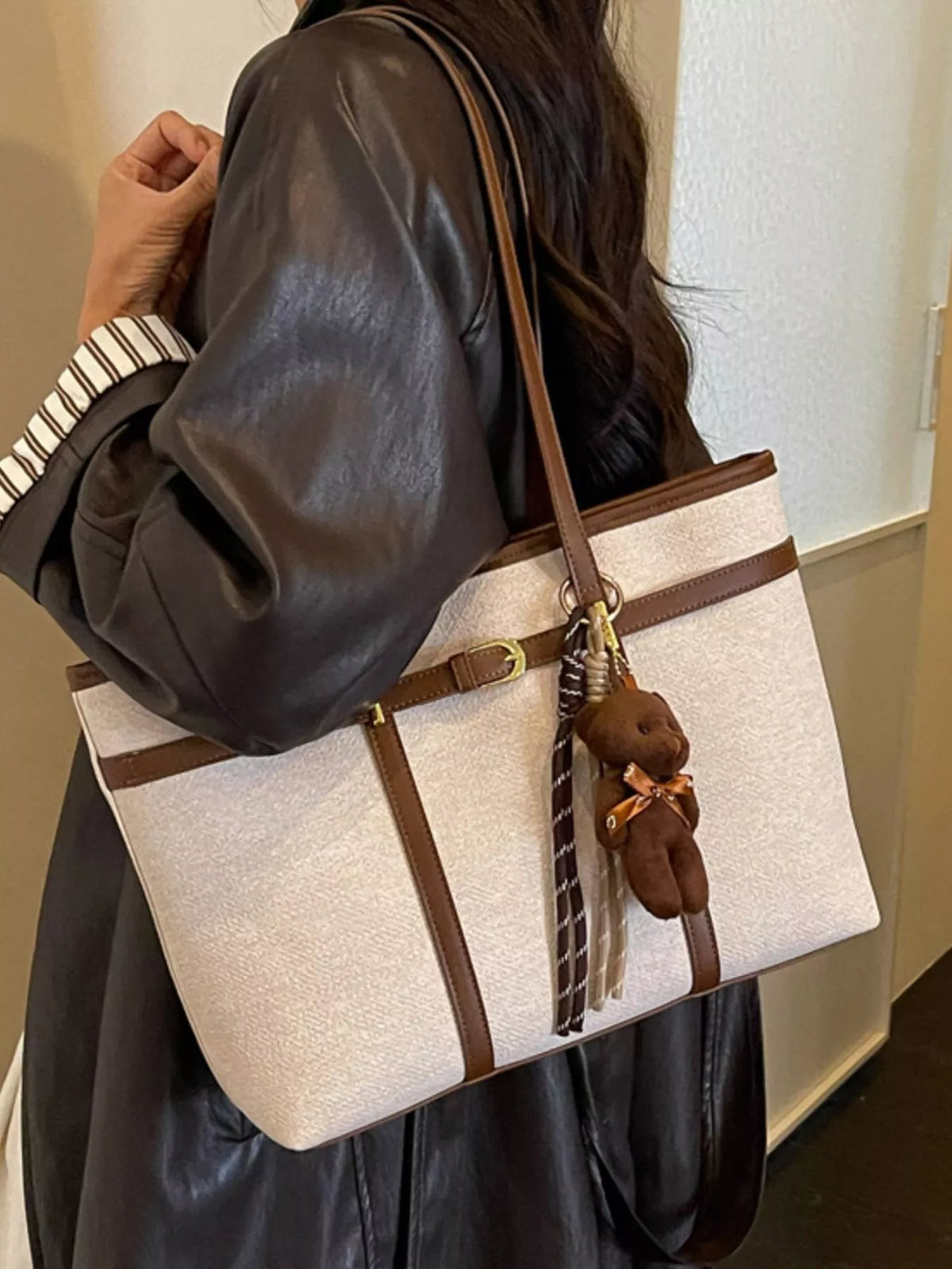 Off-white vegan leather tote bag with brown handles, center buckle strap, and teddy charm