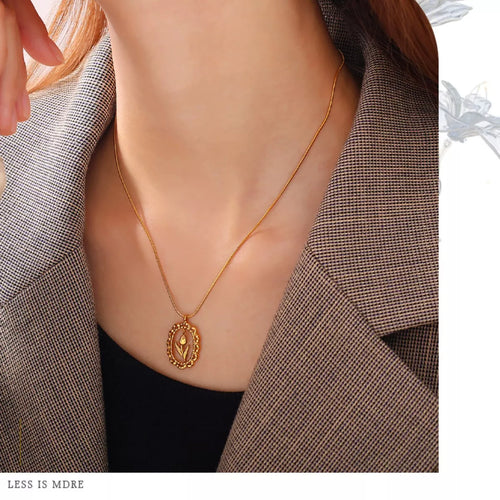 Gold-tone flower pendant necklace worn on neckline with oval charm pendant