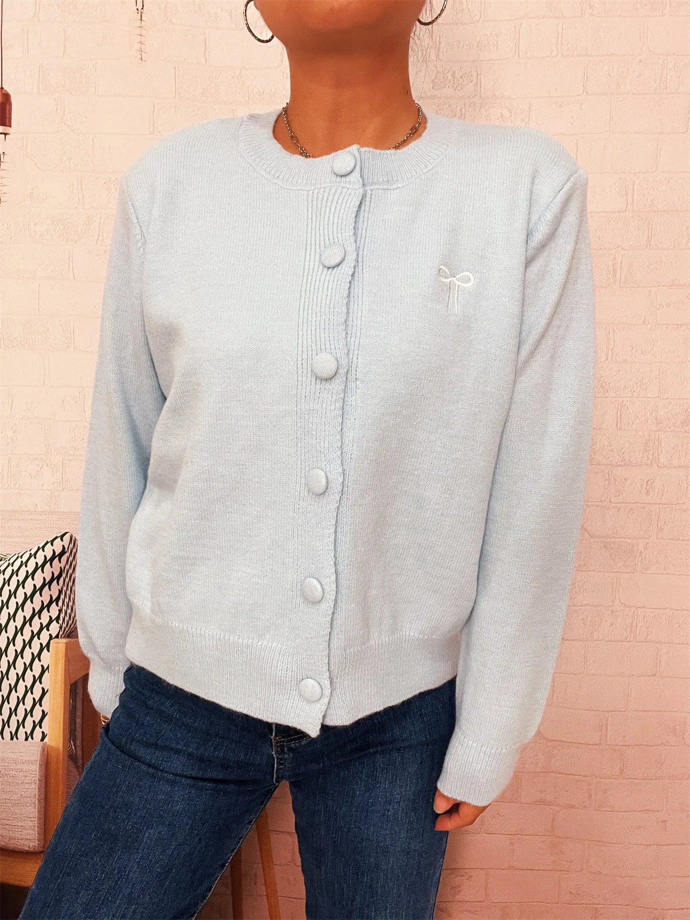 Light blue button-front cardigan with long sleeves and small bow detail on chest