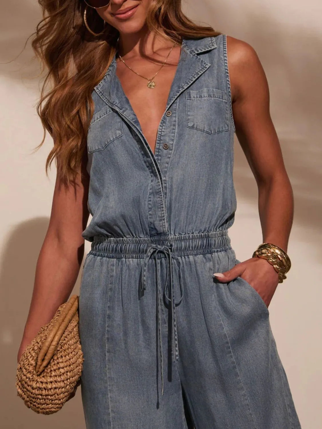 Sleeveless washed denim jumpsuit with V-neck and button front, tie-waist detail