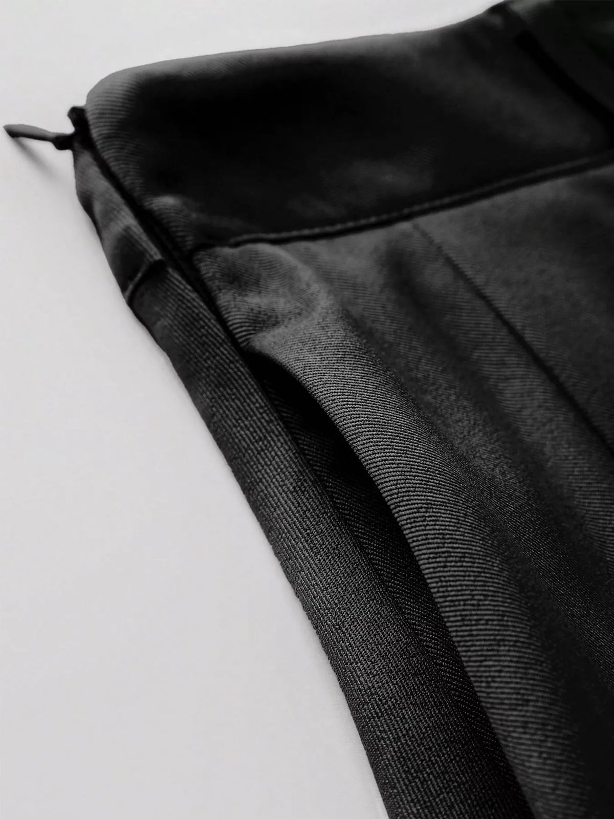 Black skirt fabric close-up with fine weave texture and crisp pleats