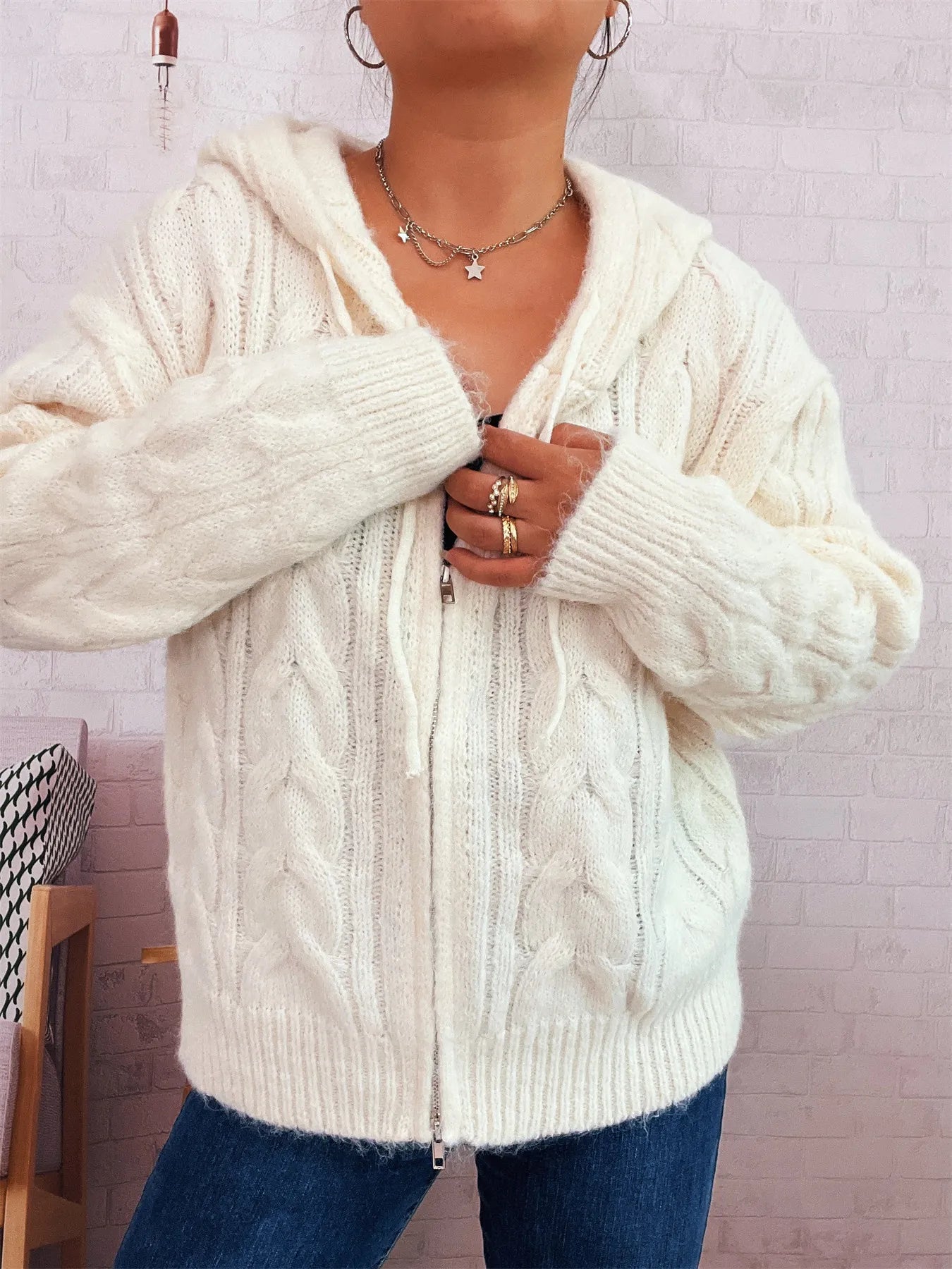 Cream cable knit hooded zip-up cardigan with front zipper and raised cable knit design.