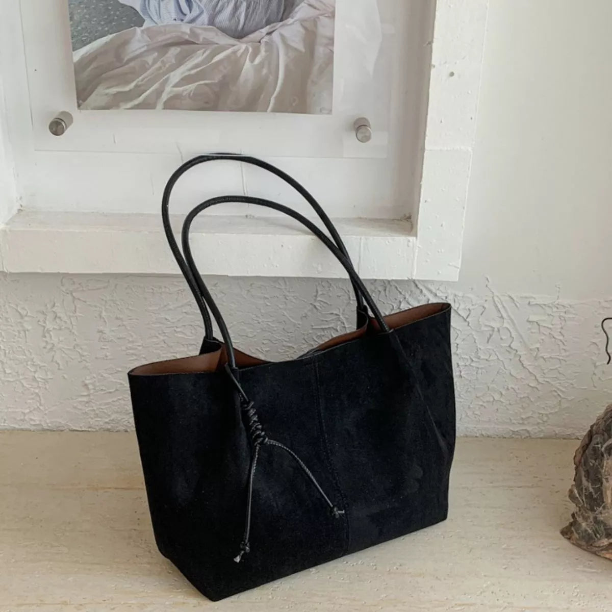 Black suede tote bag with brown-trim handles and front drawstring pocket