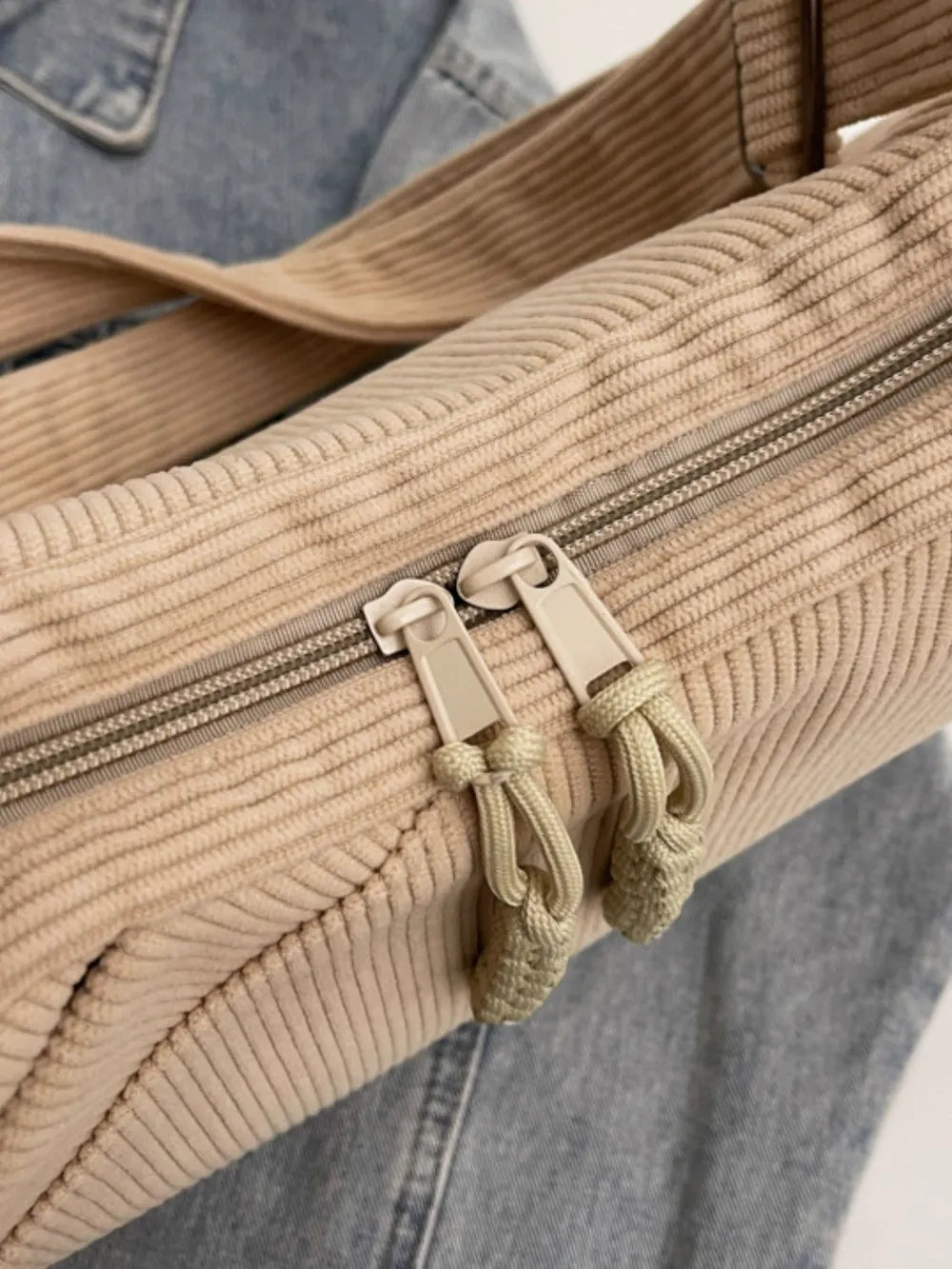 Beige ribbed hobo bag detail with zipper, tabs, and braided tassel charm