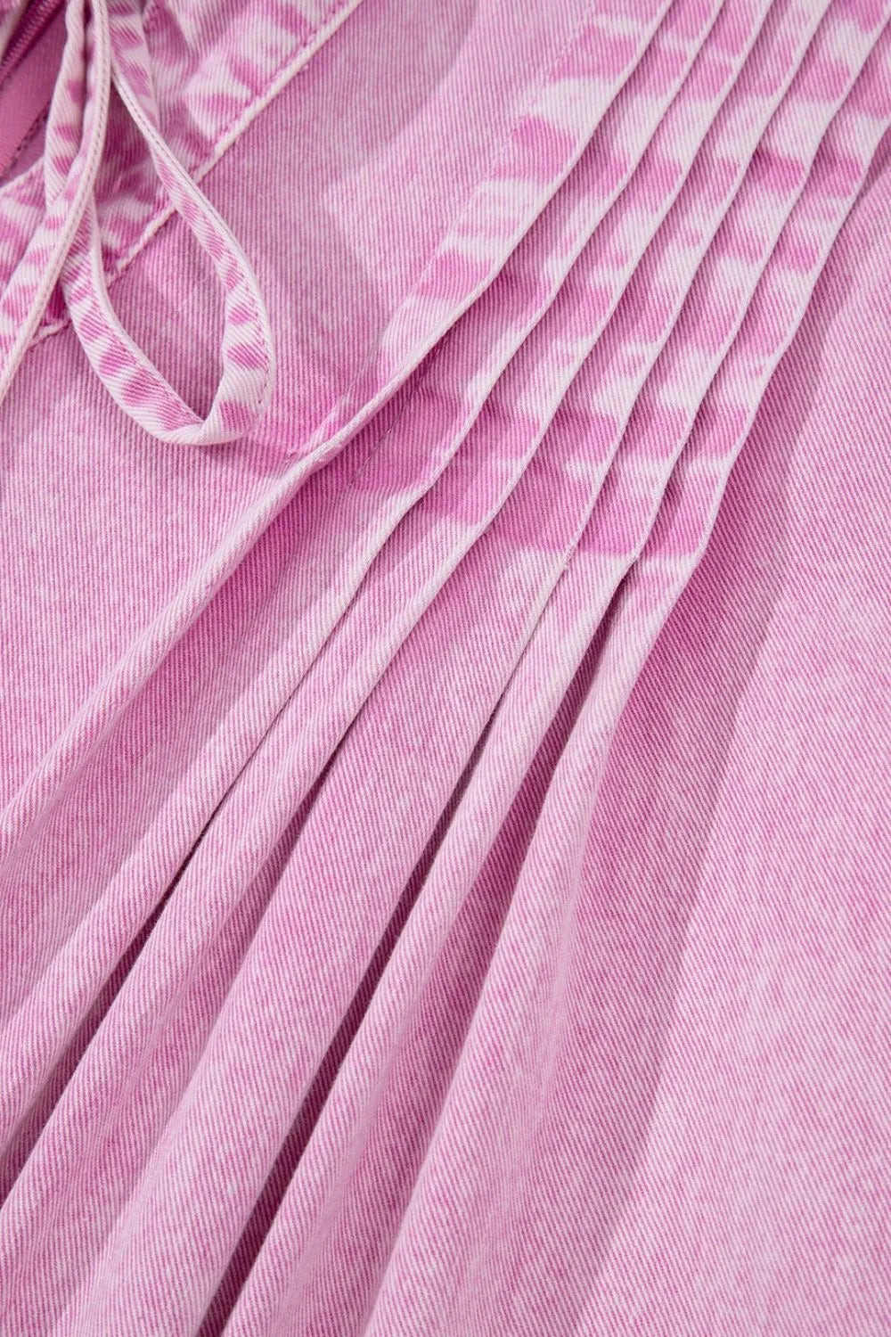 Pink mineral-wash denim romper close-up of gathered pleats on skirt front