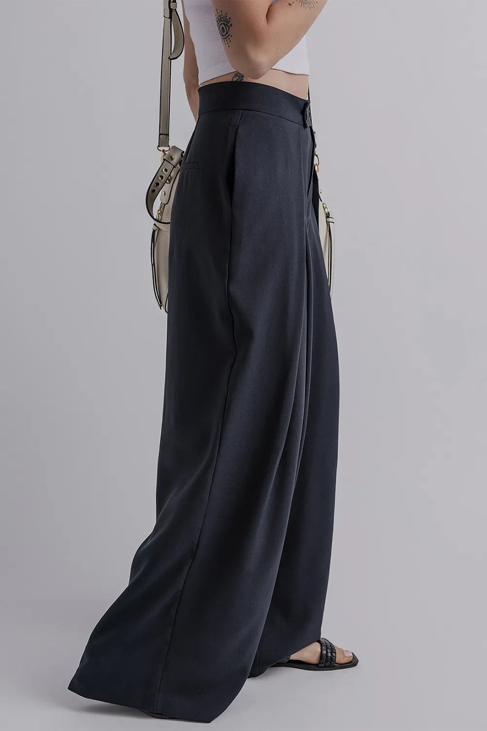 Dark navy wide-leg pants, side view with pleats and buttoned waistband pockets.