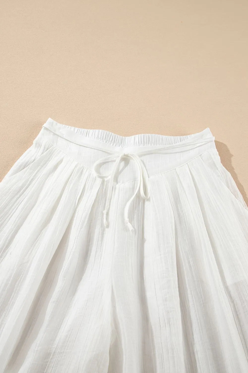 White tie-waist waistband on pleated wide-leg pants with drawstring bow detail