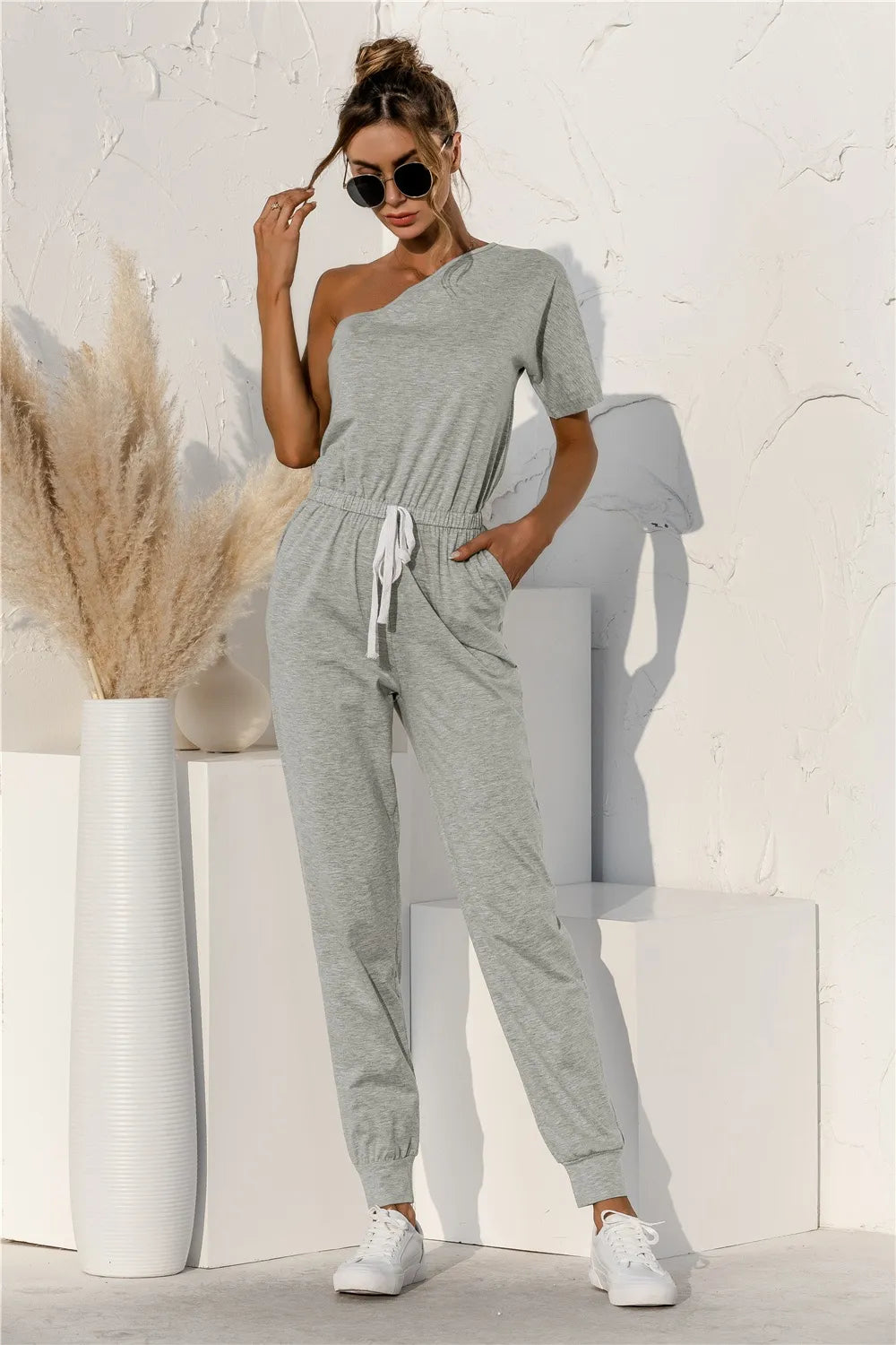Gray one-shoulder short-sleeve jumpsuit with draped neckline, tie-waist, tapered legs
