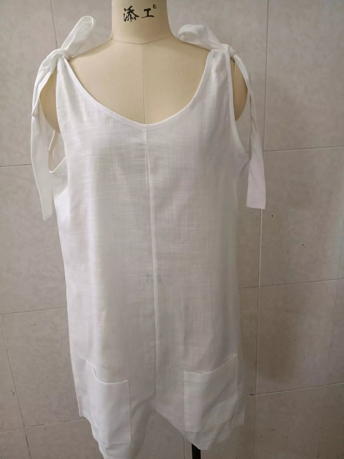 White tie-shoulder bow romper with two side pockets and back tie straps.