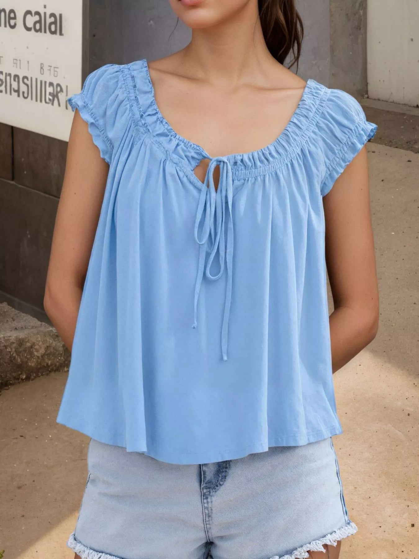 Light blue tie-front blouse with ruffled cap sleeves and center drawstring tie at neckline