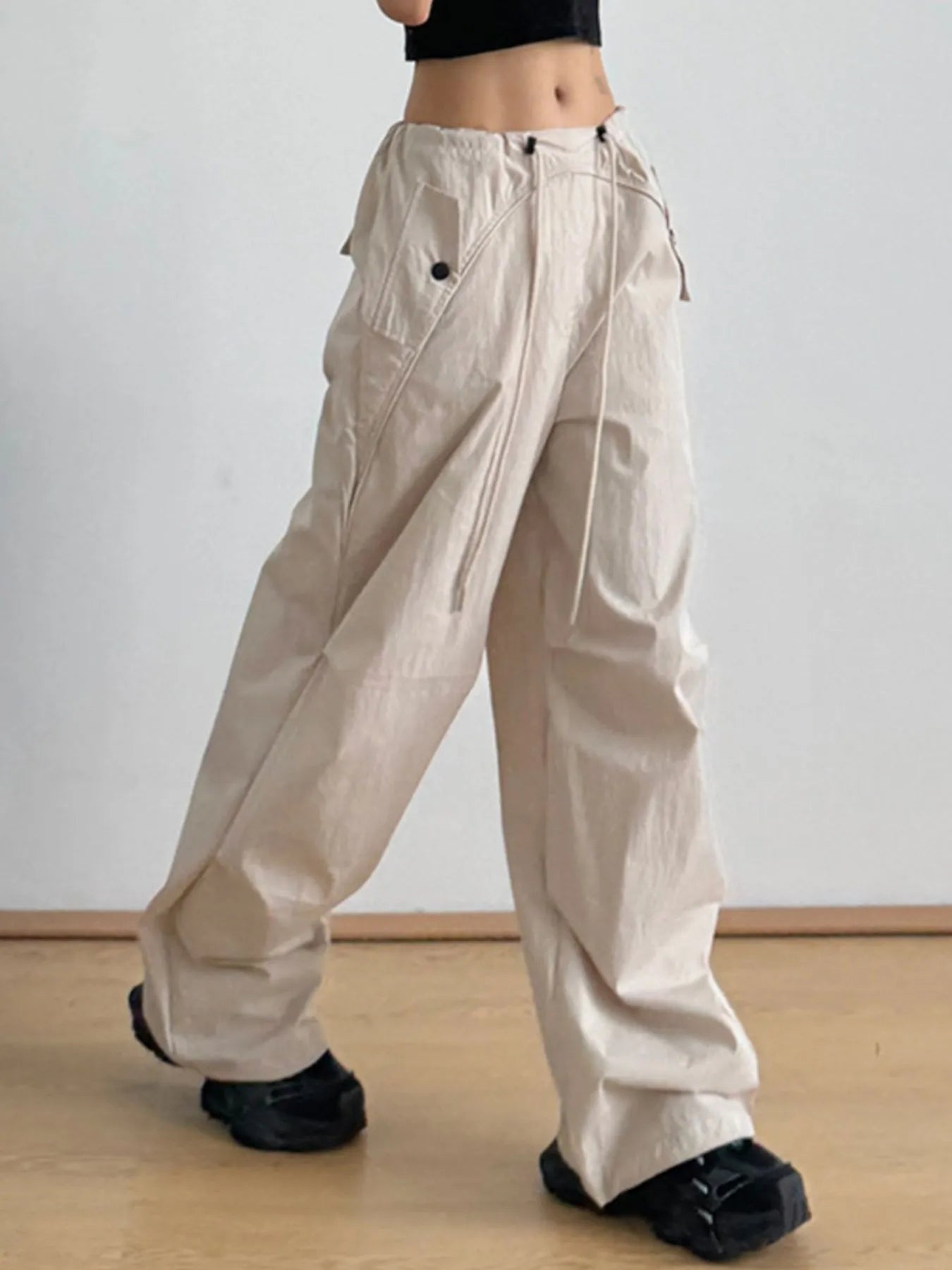 Beige relaxed wide-leg drawstring pants with buttoned side tabs and ankle pleats
