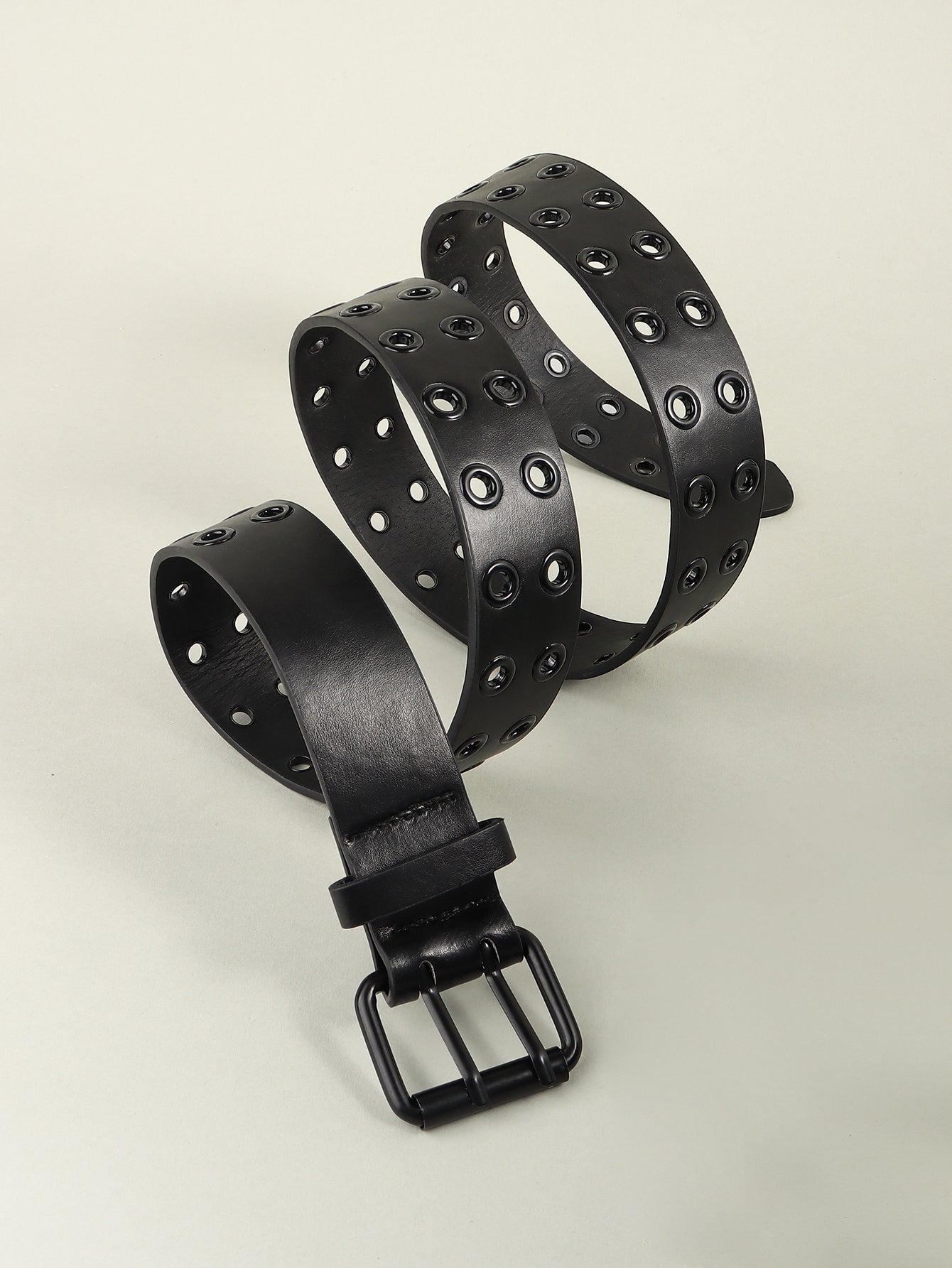 Black vegan leather grommet belt shown coiled, with square buckle at bottom.
