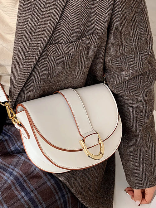 White half-moon crossbody bag with buckle flap, gold-tone hardware, adjustable strap